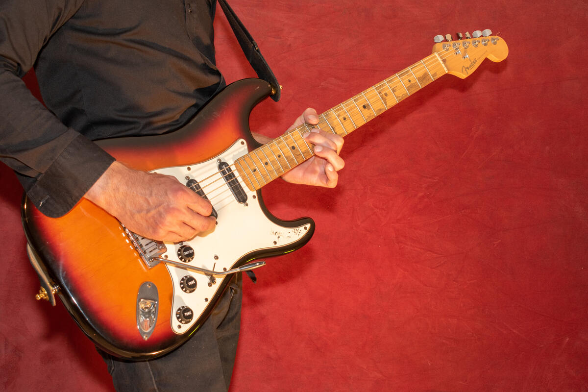 Man play a sunburst Fender Stratocaster.