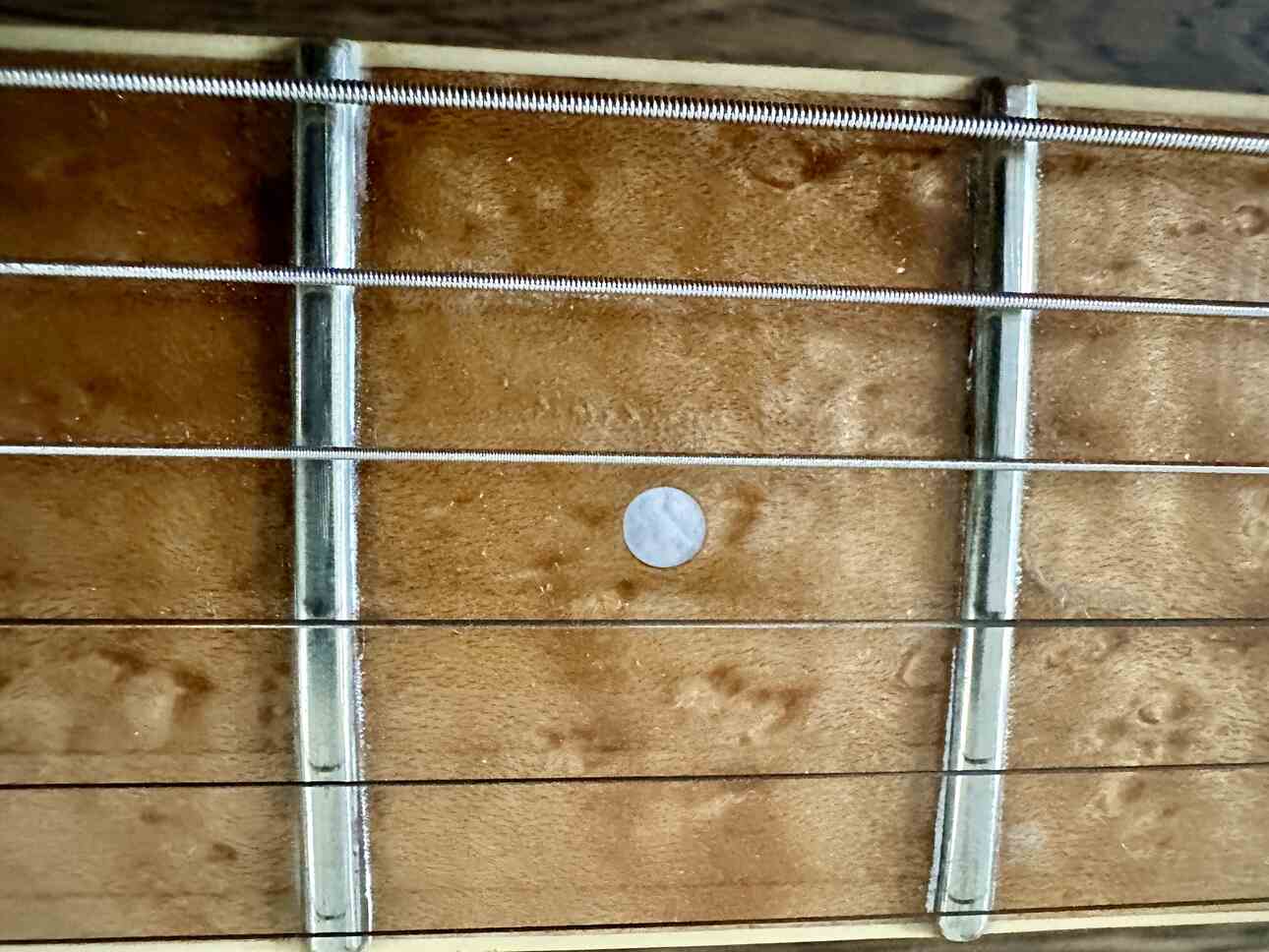 Closeup of two frets on a birdseye maple guitar neck, seen from above.