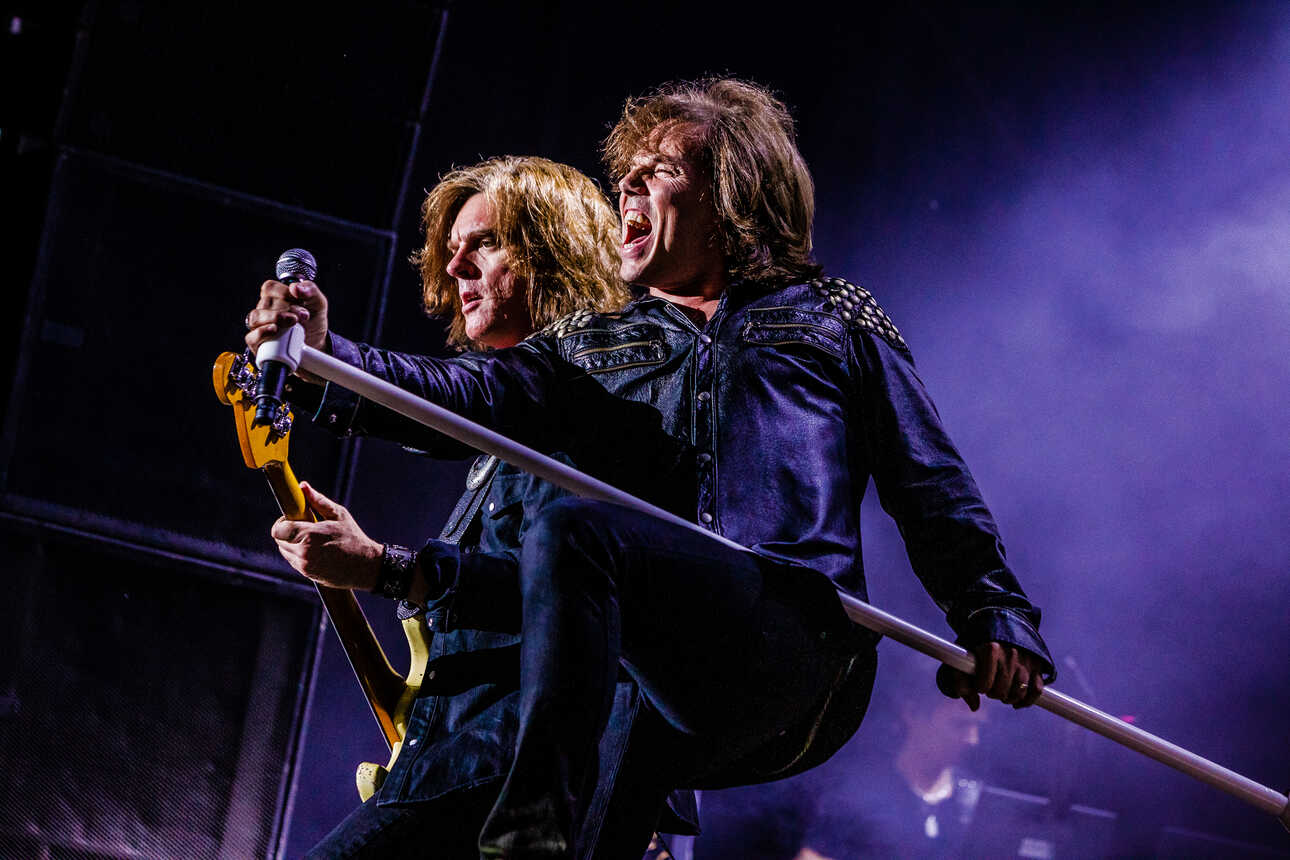 Europe live on stage with singer Joey Tempest holding his long microphone stand stretched out before him.