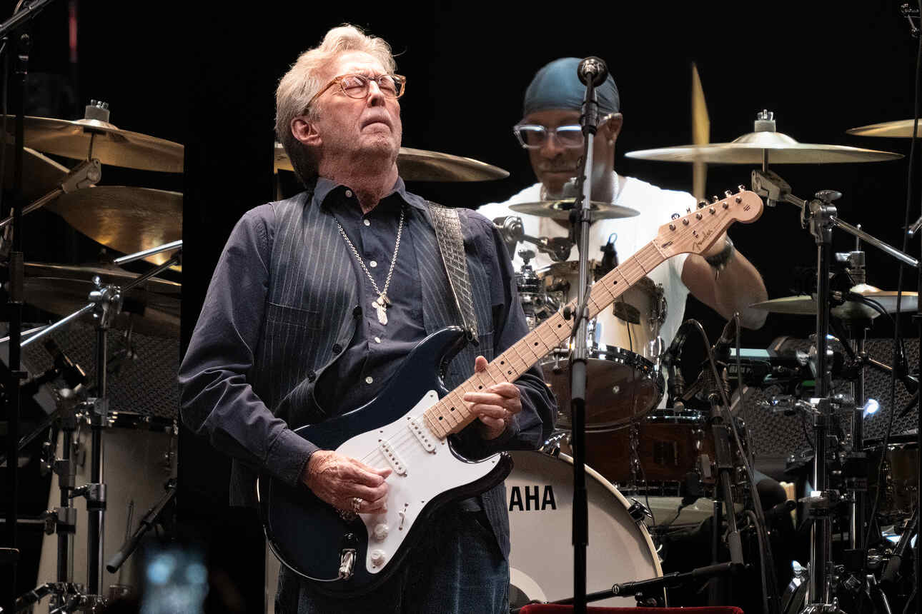Guitarist Eric Clapton on stage in the Detroit Little Ceasar's Arena while playing a black Fender Stratocaster.
