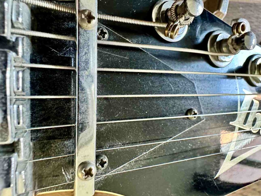 Closeup of a black, plastic truss rod cover near the headstock on a Ibanez Universe 7-string guitar.