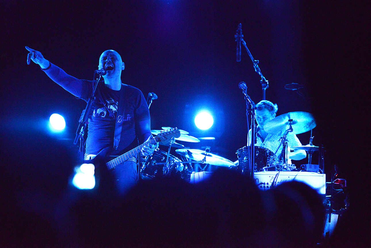 Billy Corgan, in blue light, live on stage with The Smashing Pumpkins.