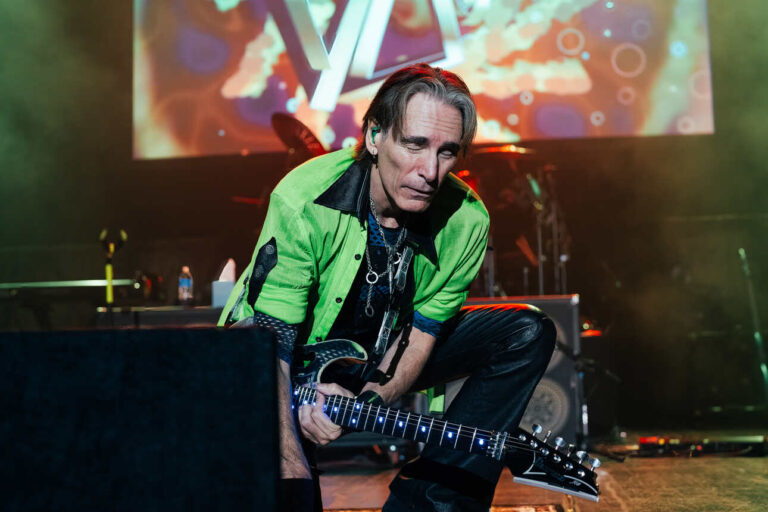 Steve Vai kneels down near a monitor speaker during a live performance in Detroit, Michigan.