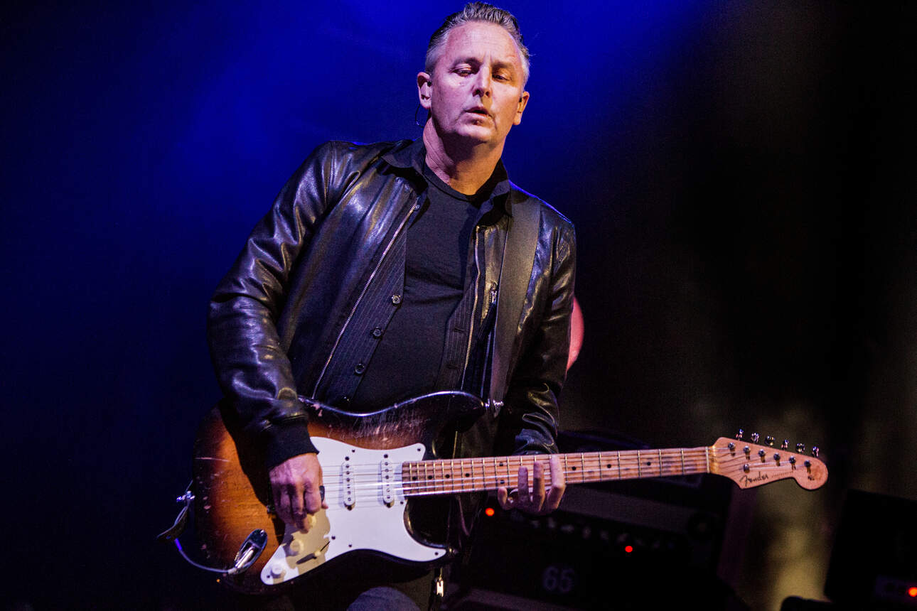 Pearl Jam's Mike McCready wearing a black leather jacket while playing his sunburst Fender Stratocaster on stage.