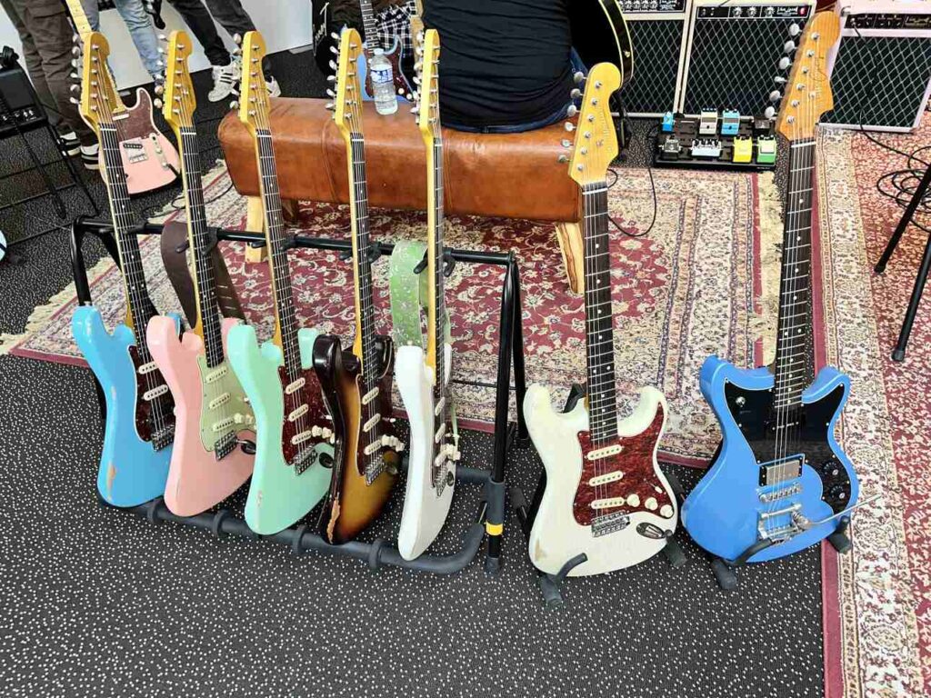 Five guitars with different finishes in a rack with two extra electric guitars to the right.