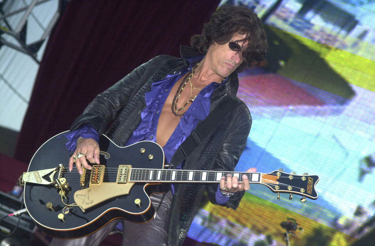 Guitarist Joe Perry of Aerosmith playing a dark blue Gretsch semi-acoustic guitar.